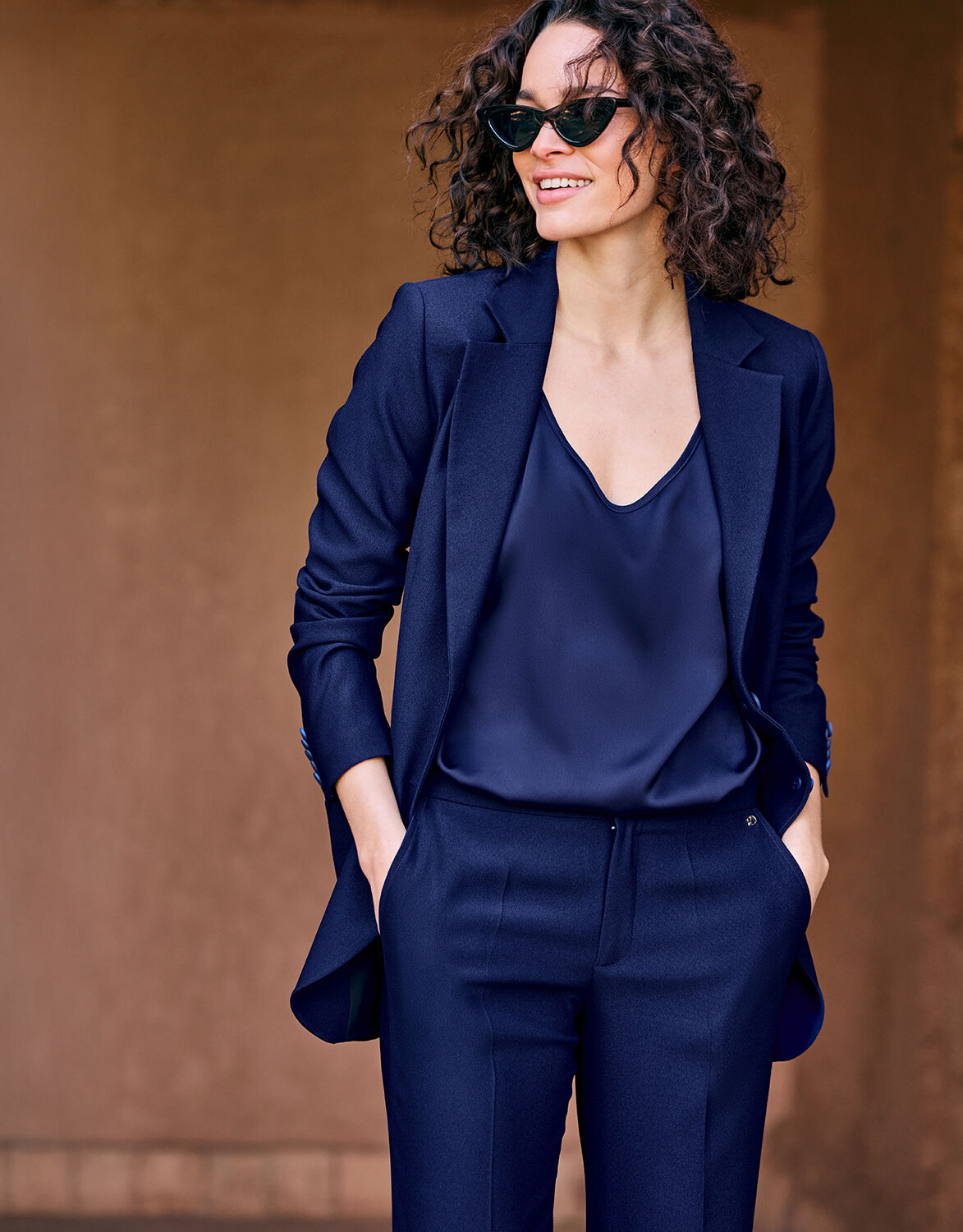 Model standing in the Carey Sapphire Blue blazer in crepe satin over a satin top and trousers.