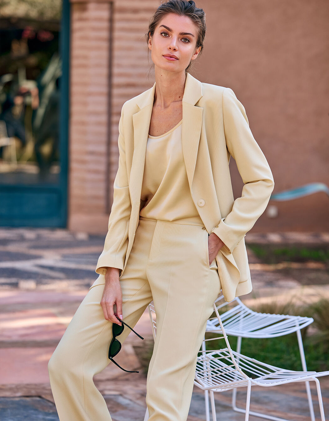 Model standing in the Carey Buttery yellow blazer in crepe satin with a matching top and trousers.
