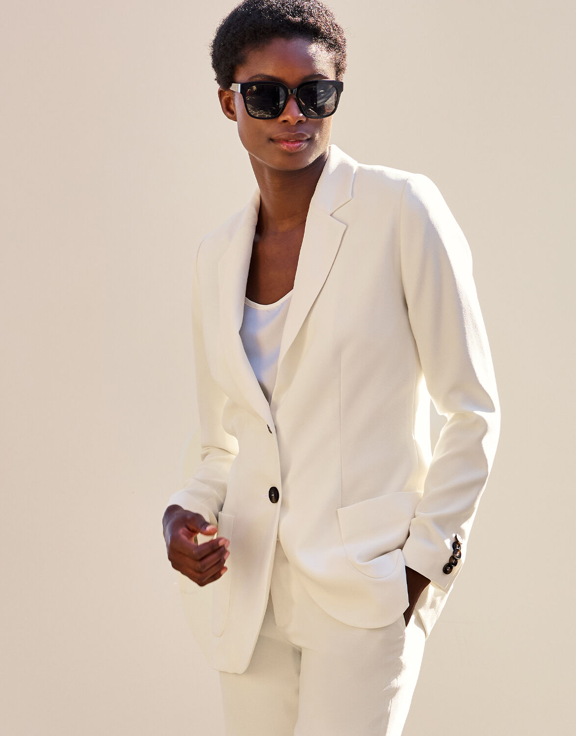 Model standing in the Carey Ivory blazer in crepe satin, worn with a white top and matching trousers.