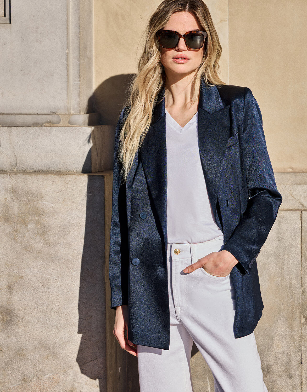 Model standing in the Halle Midnight Blue Satin blazer in crepe satin with white jeans.