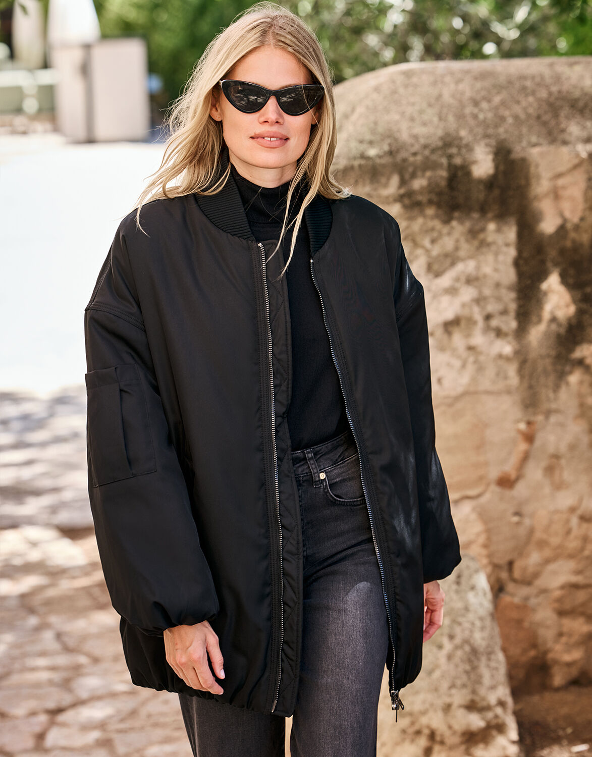 Model standing in the Julie Black jacket in woven, an oversized bomber style.