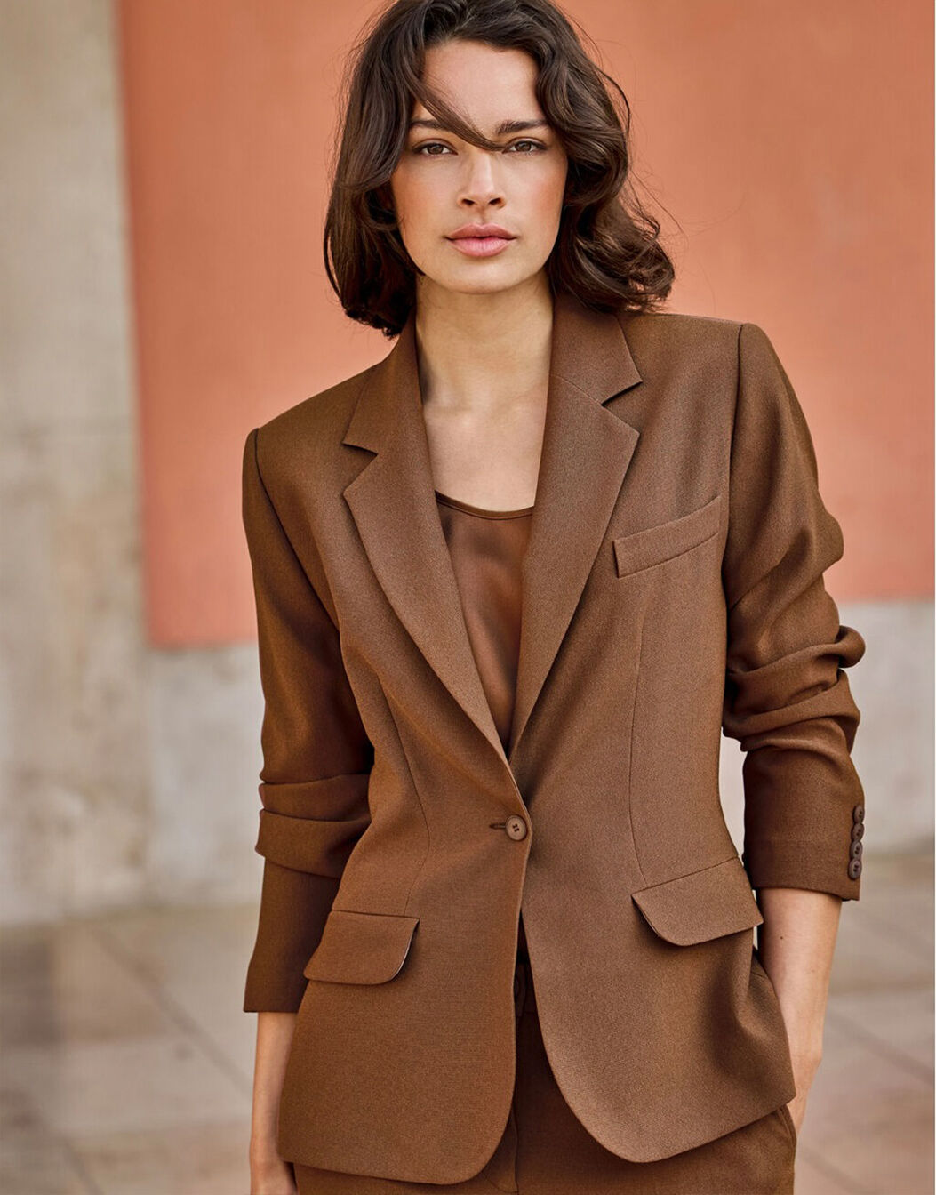 Model standing in the Nadia Cacao Brown blazer in crepe satin with a satin top.