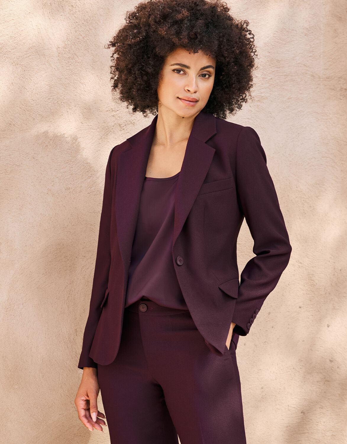 Model standing in the Nadia Deep Aubergine blazer in crepe satin with matching trousers.