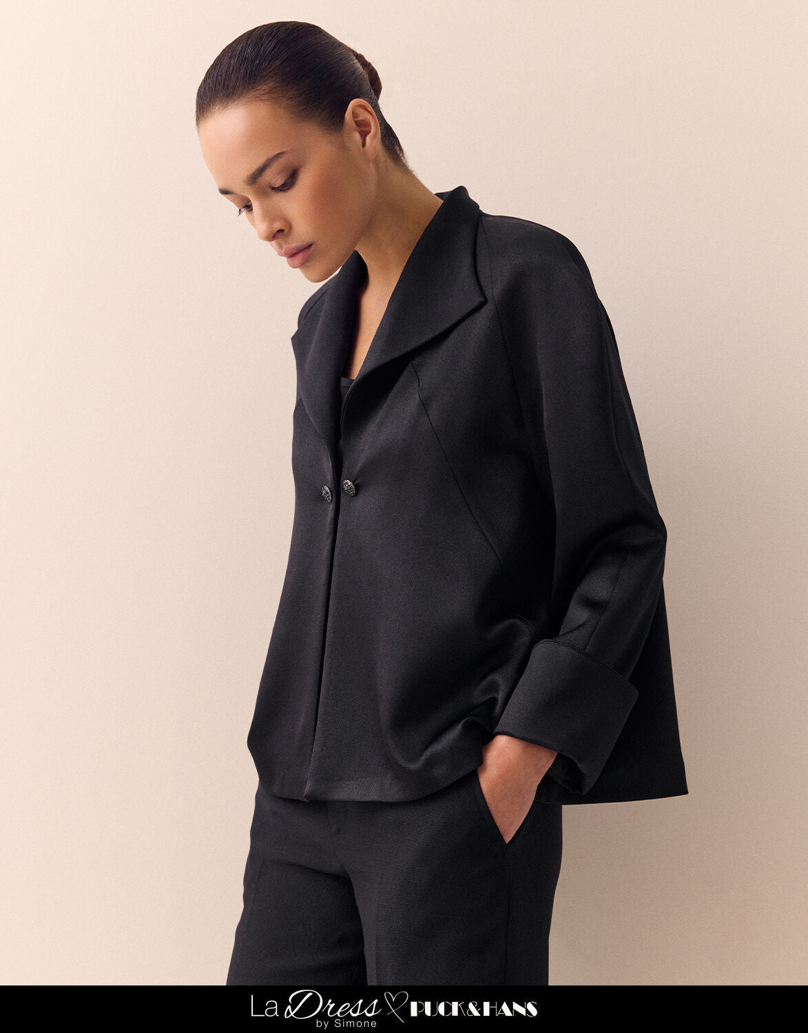 Model standing in the Sao Paulo Black Satin jacket in crepe satin with a wide collar.