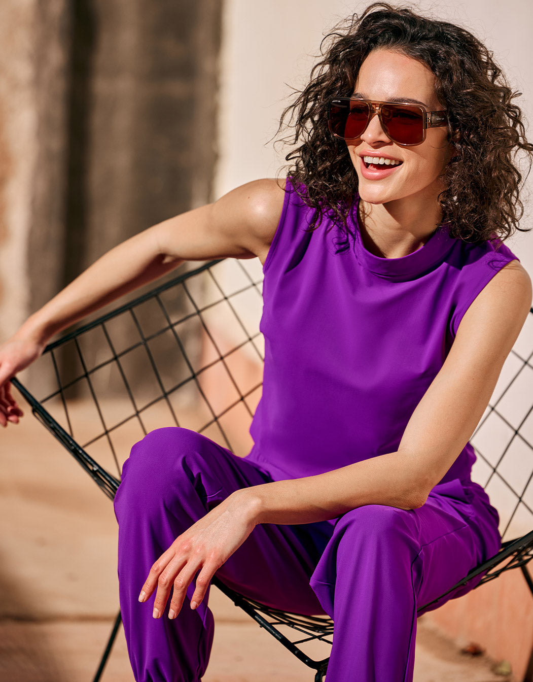 Model seated outdoors in the Amber Violet sleeveless top with matching purple trousers.