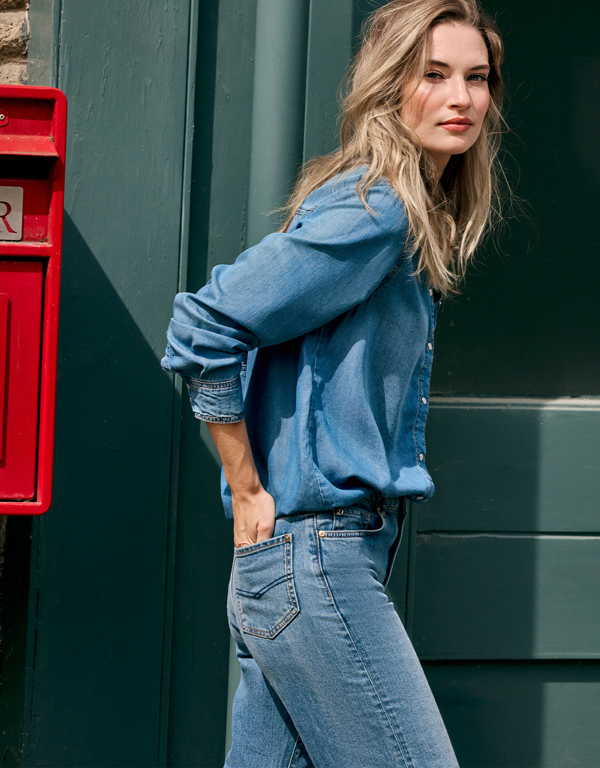 Model leaning against a green door in the Andrea Light Indigo denim shirt and jeans.