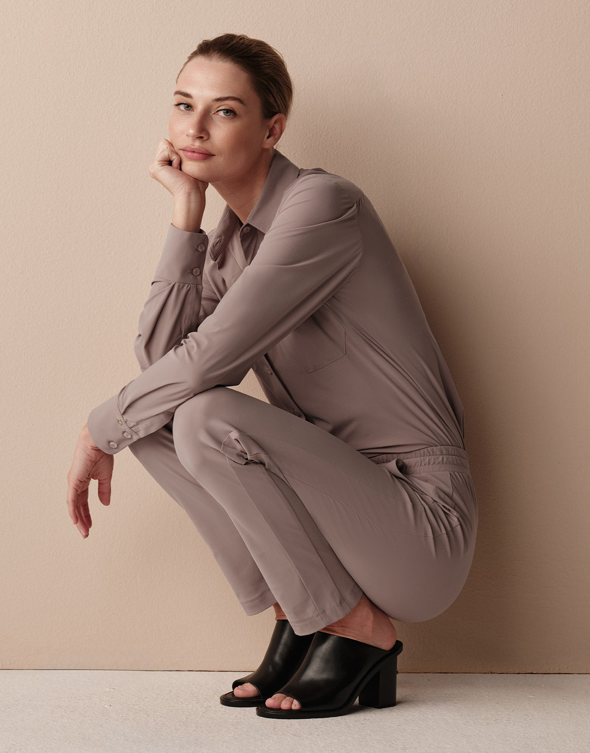 Model crouching in the Annie Soft Taupe jersey lycra shirt with matching taupe trousers.