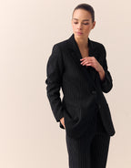 Model standing in the Bombay Black blazer in stretch woven with pinstripes and matching trousers.