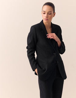 Model standing in the Bombay Black blazer in stretch woven with pinstripes and matching trousers.