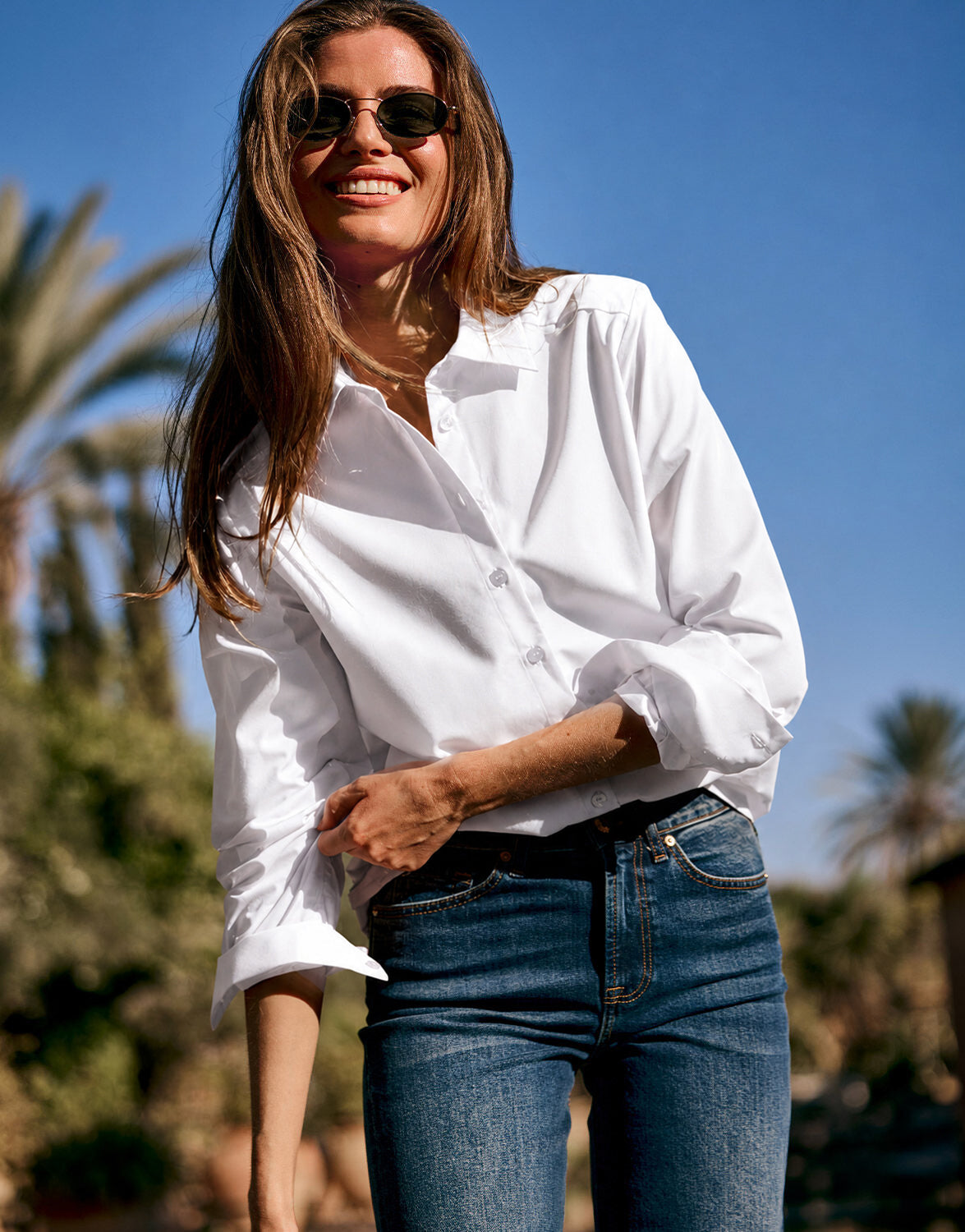 Model standing in the Cameron White blouse in poplin, worn with jeans and sunglasses.