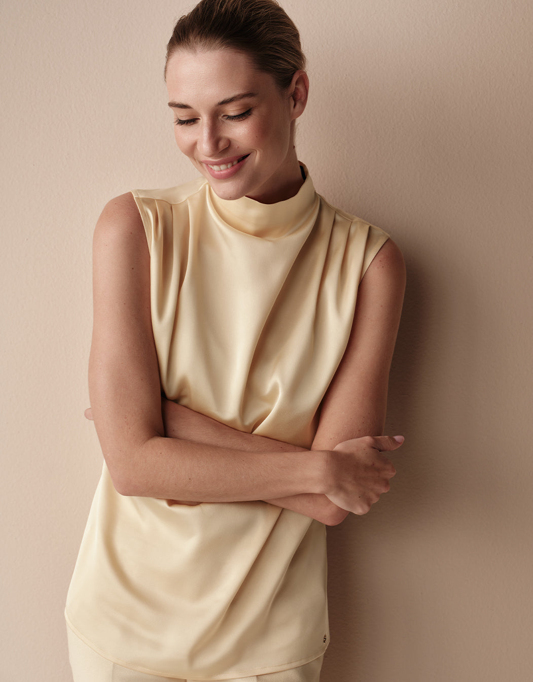 Model standing in the Chrissy Buttery Yellow blouse in satin, sleeveless with a high neck.