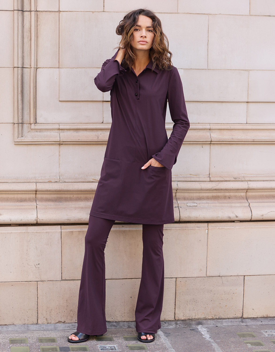 Model standing in the Eleanor Deep Aubergine tunic in jersey lycra over matching trousers.