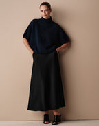 Model steht im Milou Black Satin Rock aus Crêpe-Satin mit dem Emmy Midnight Blue Pullover.