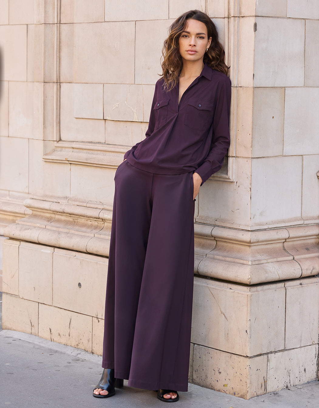 Model leaning in the Savona Deep Aubergine trousers in jersey lycra with a matching blouse.