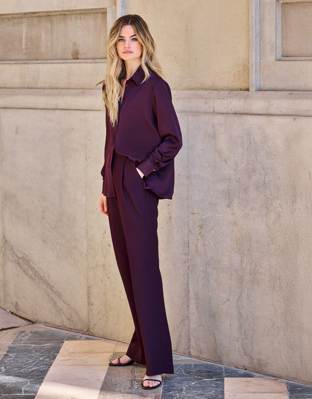 Model standing in the Torino Deep Aubergine trousers in crepe satin with a matching blouse.