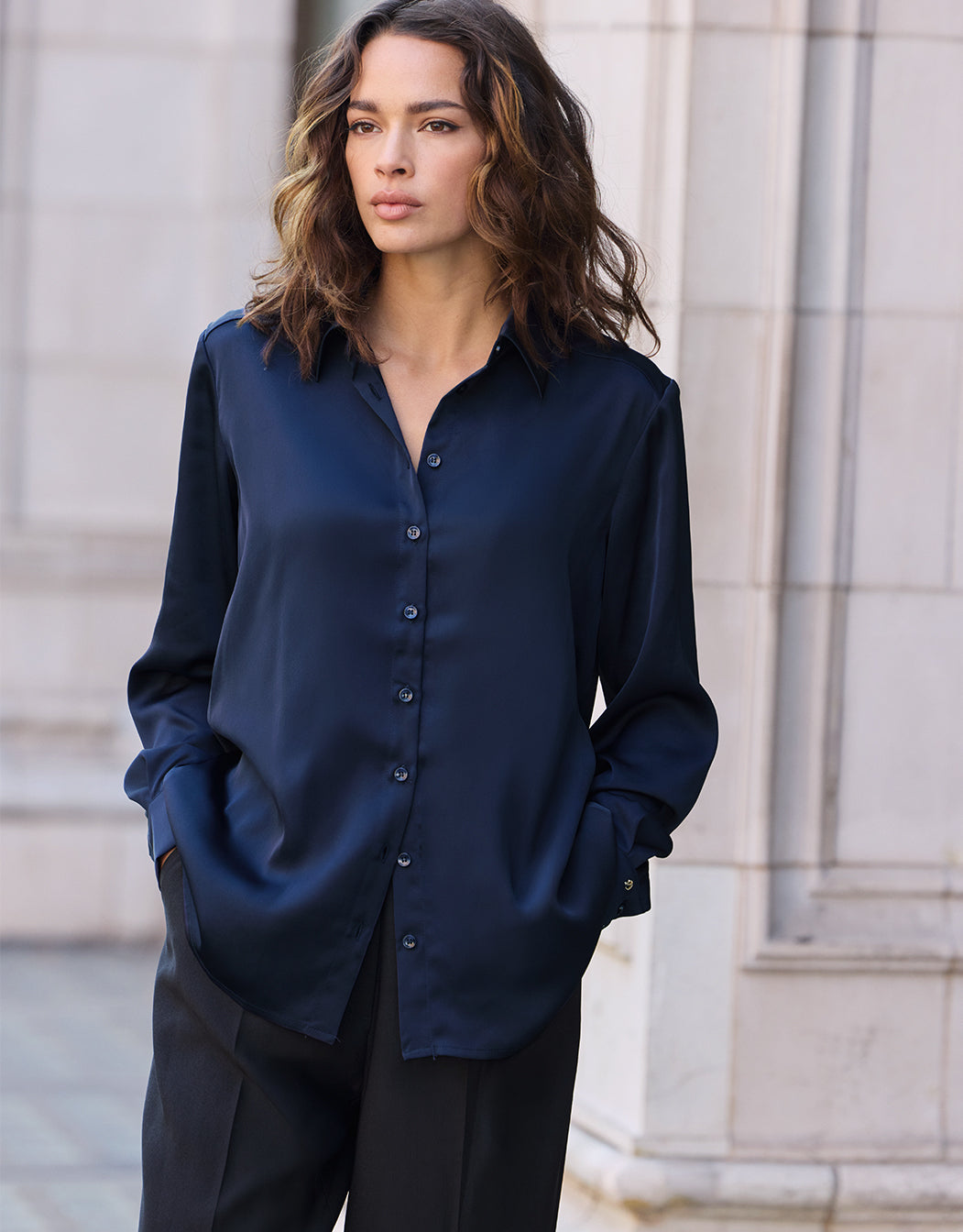 Model standing in the Estee Midnight Blue blouse in satin with black trousers.