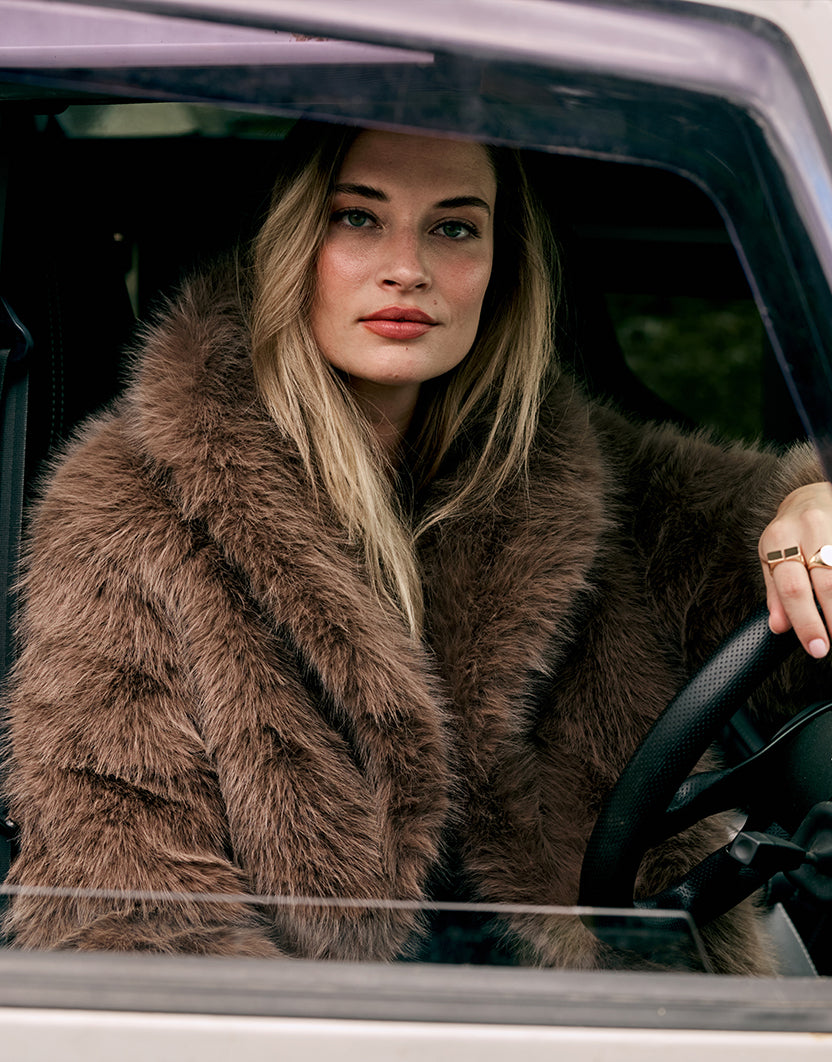 Model sitzt in einem Auto im Isolde Dark Taupe Mantel aus Kunstfell, eine Nahaufnahme.