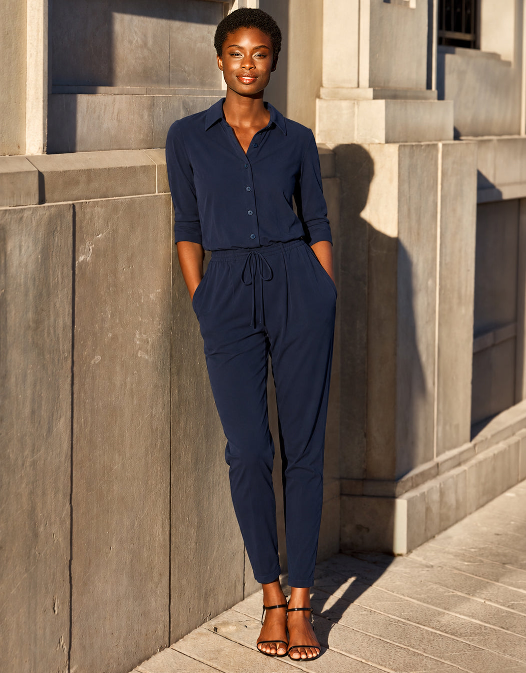 Model steht im Jade Midnight Blue Jumpsuit aus Jersey Lycra mit einem Kragen und Tunnelzugbund.