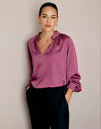 Model standing in the Jolie Plum blouse in satin with a stand collar and black trousers.