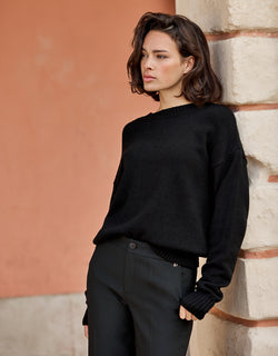Model leaning in the Lucienne Black jumper in viscose knit with black trousers.
