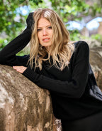 Model leaning in the Lucienne Black jumper in viscose knit against a tree.