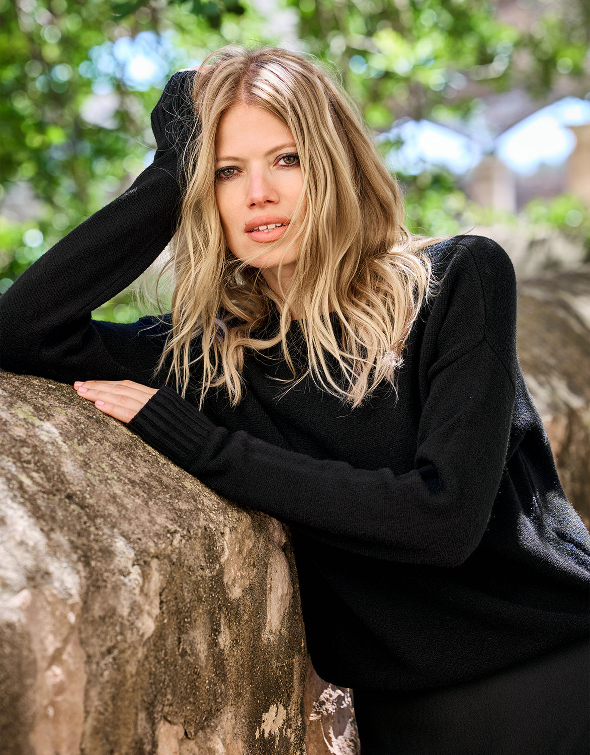 Model leaning in the Lucienne Black jumper in viscose knit against a tree.