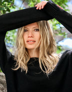 Model standing in the Lucienne Black jumper in viscose knit with the arms raised.