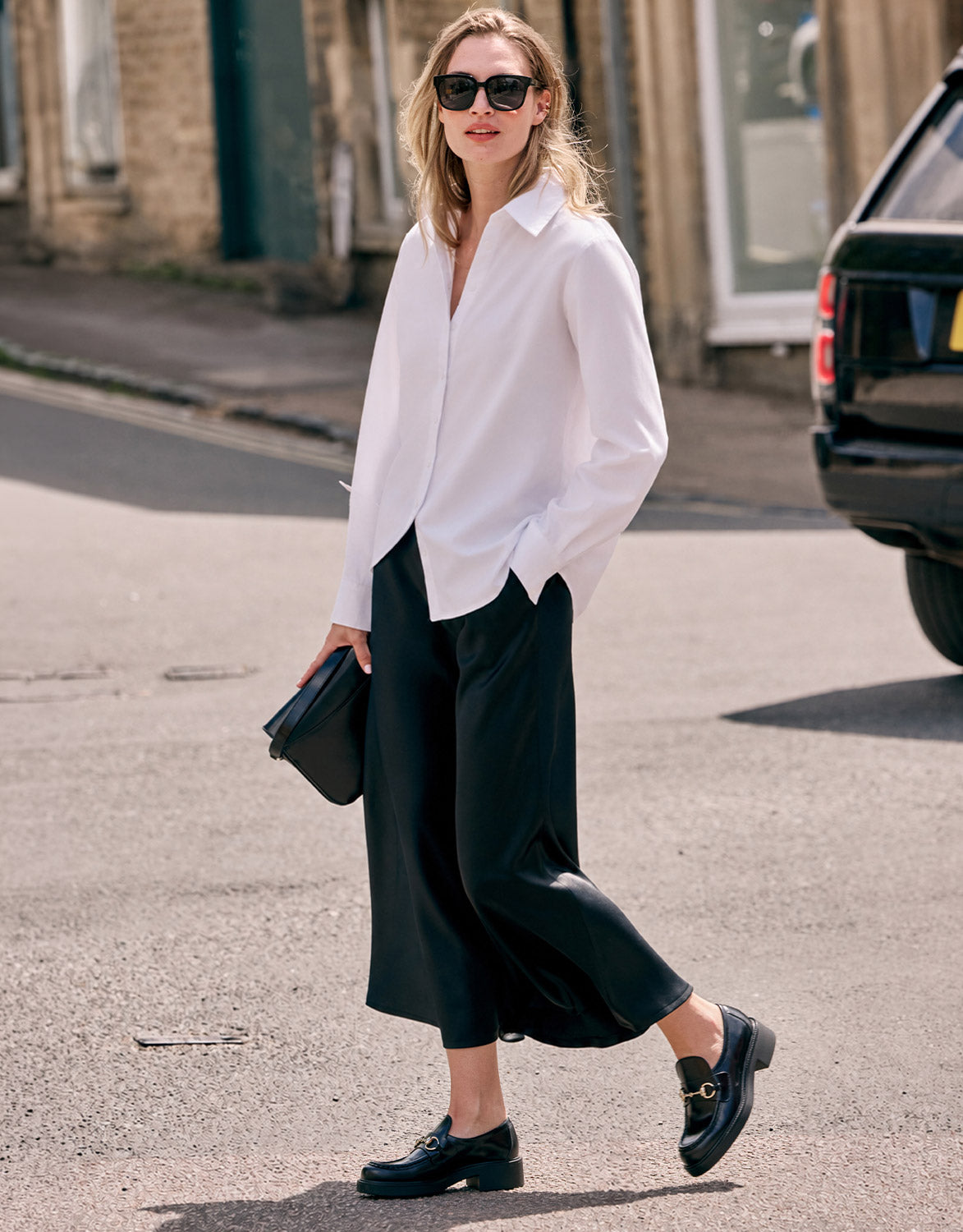 Model walking in the Milou Black Satin skirt in crepe satin with the Cameron White blouse.