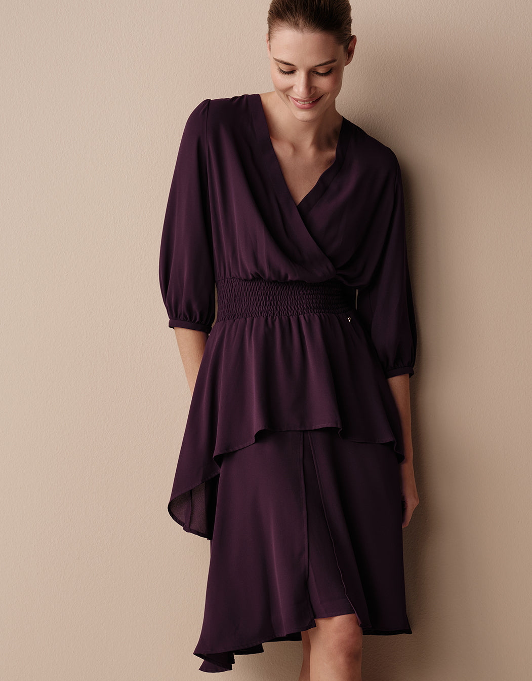 Model standing in the Rue Deep Aubergine dress in crepe georgette with a wrap front.