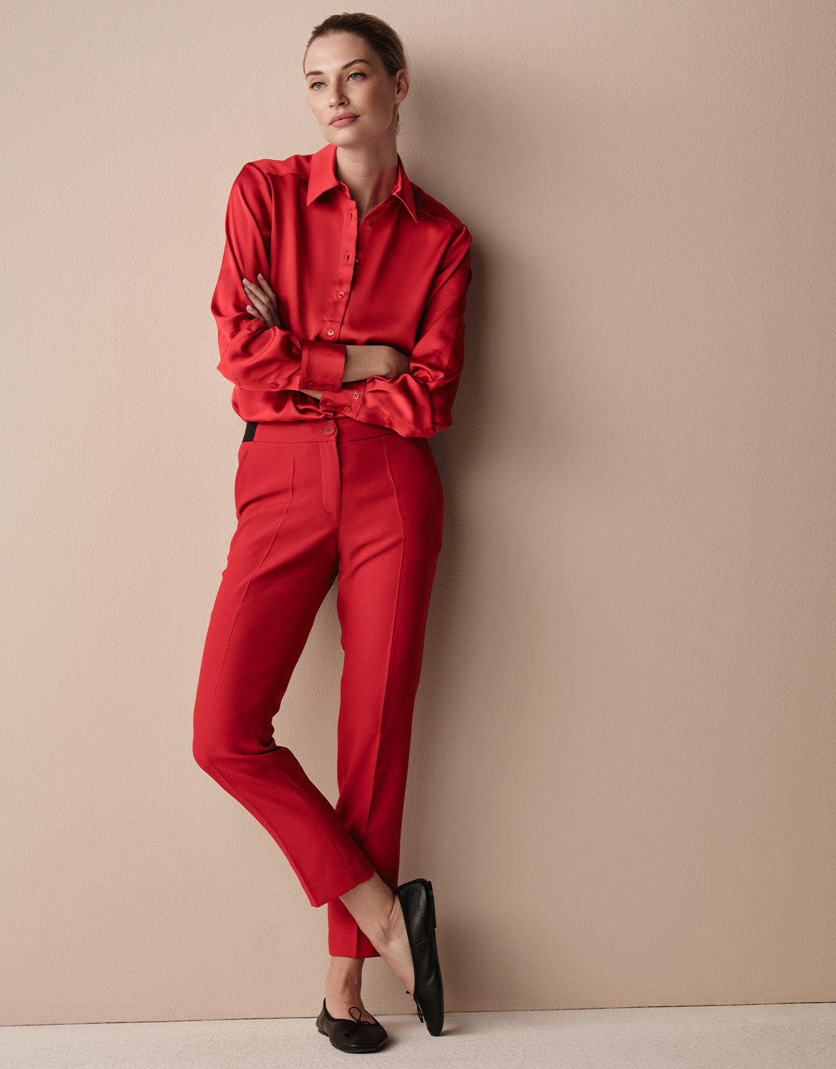 Model leaning in the Seoul Raspberry Red trousers in crepe satin with a satin blouse.
