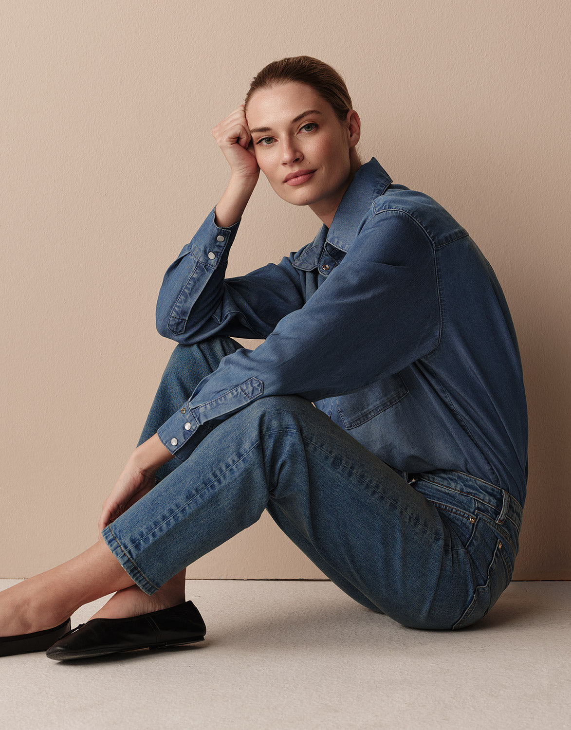 Model seated in the Sigrid Light Indigo blouse in lyocell denim with jeans and flats.