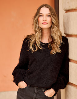 Model leaning in the Stefania Black jumper in alpaca blend with dark jeans.