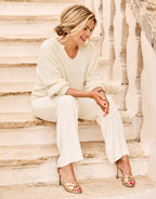 Model seated on stone steps in the Stefania Ivory jumper in alpaca blend with ivory trousers.
