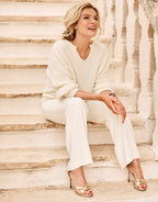 Model seated in the Stefania Ivory jumper in alpaca blend with ivory trousers and gold sandals.