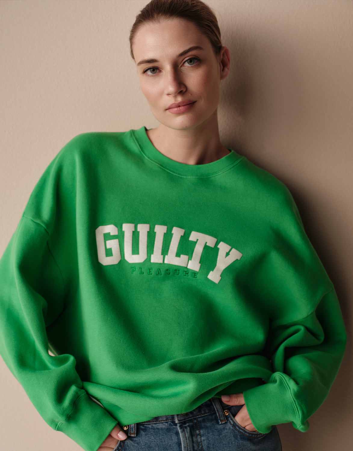 Model standing in the Story Sweater Bright Green in organic cotton knit with a GUILTY print.