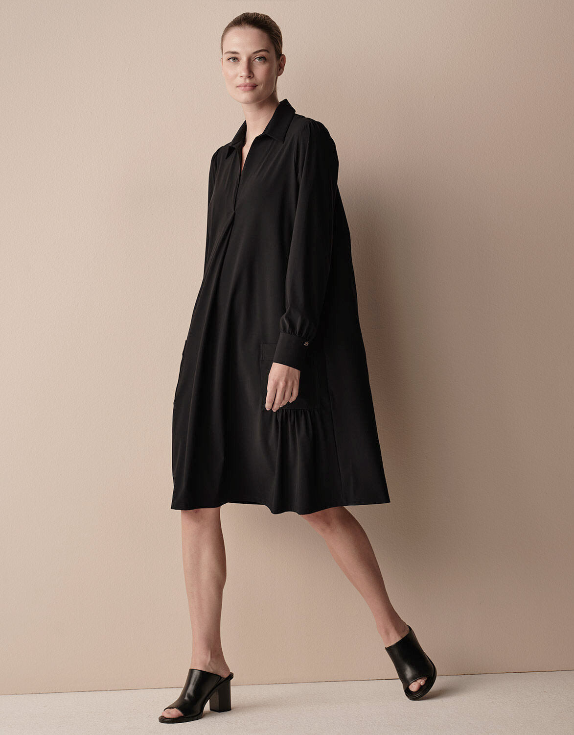 Model walking in the Therese Black dress in jersey lycra with a collar and tie belt.
