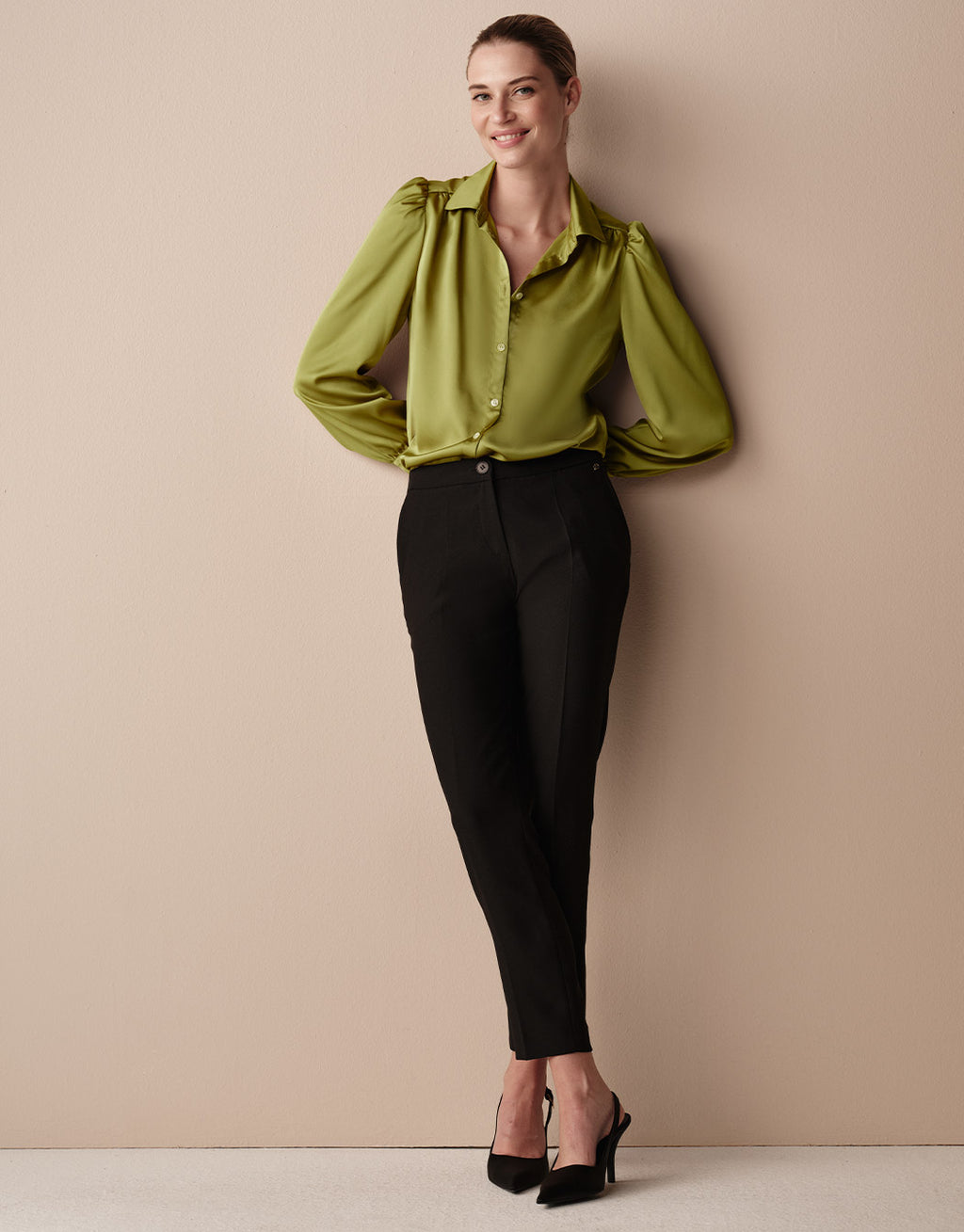 Model standing in the Tilda Lime blouse in satin with black tapered trousers.