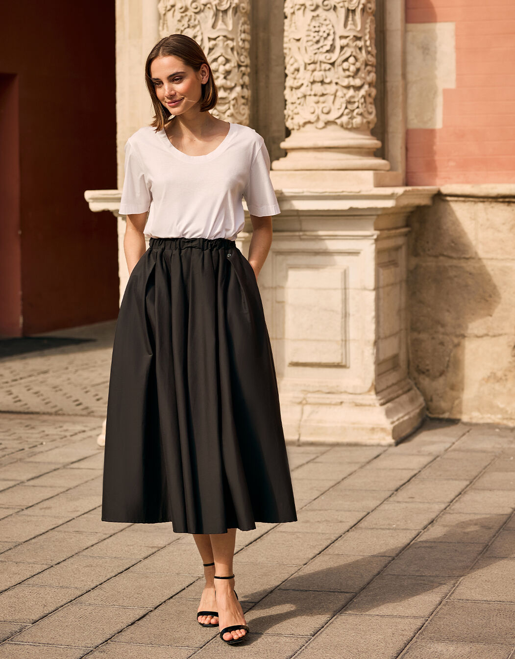 Model standing in the Thea Black skirt in cotton stretch poplin with a white T-shirt.