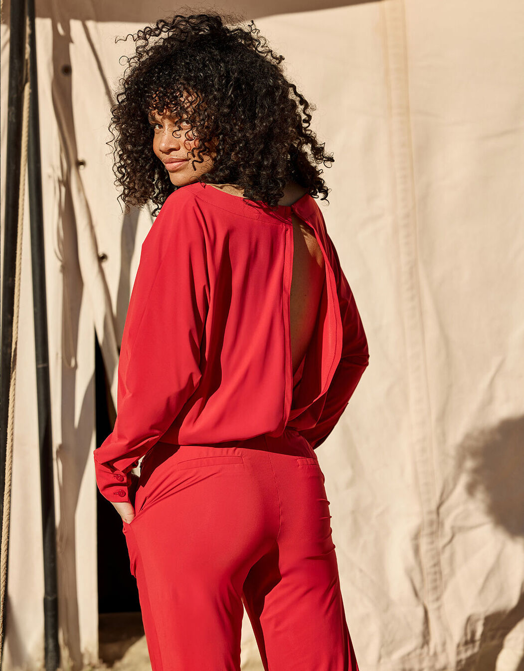 Model standing in the Lucille Raspberry Red jumpsuit in jersey lycra with an open back.