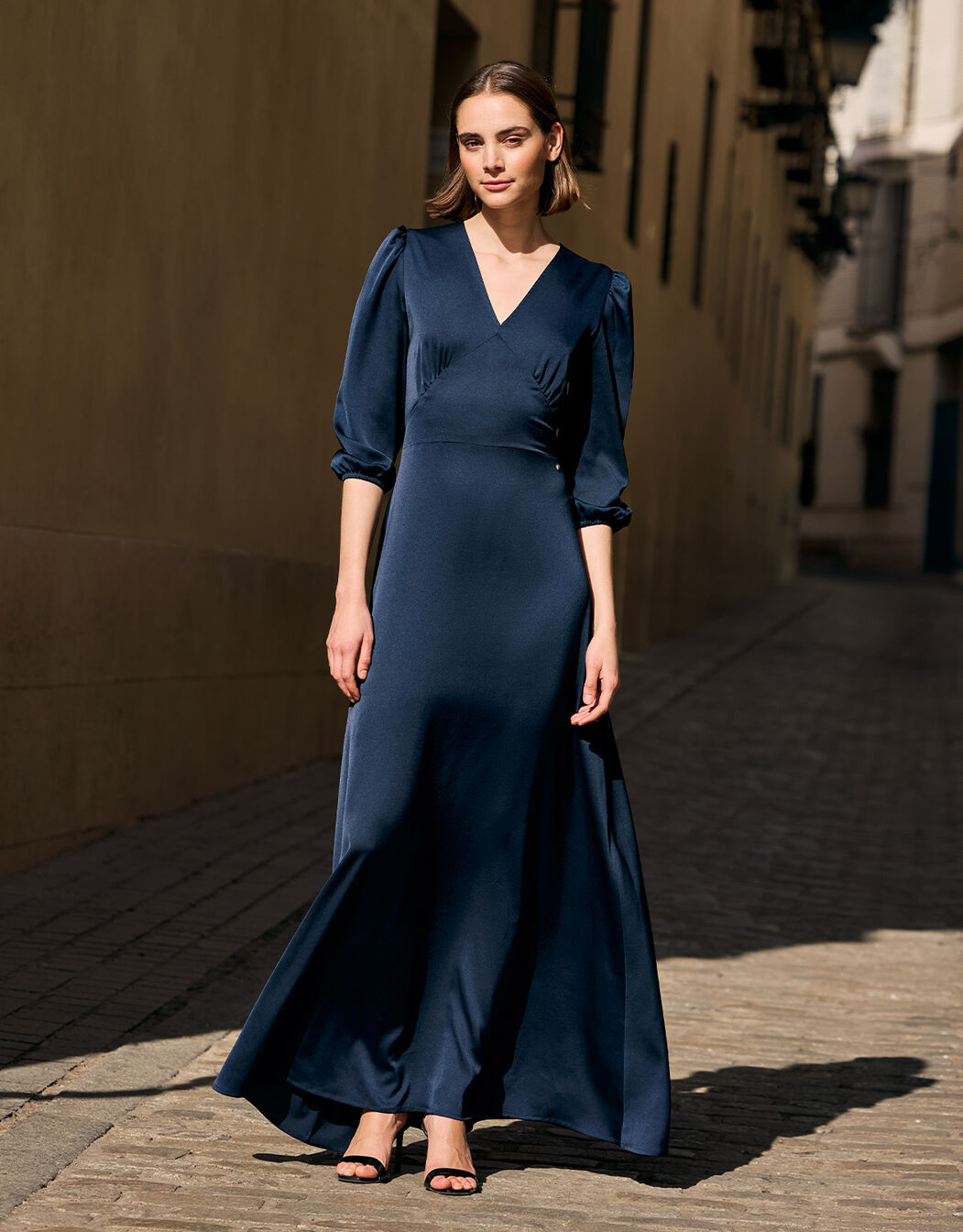 Model in a sunlit street wearing the Alyssa Midnight Blue satin maxi dress.