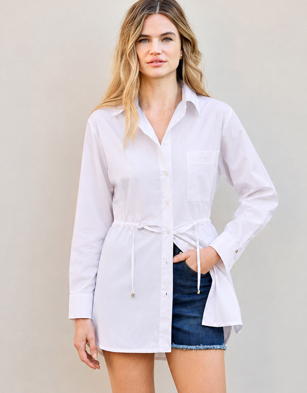Model standing in the Carrie White blouse in poplin, worn long over a denim skirt.