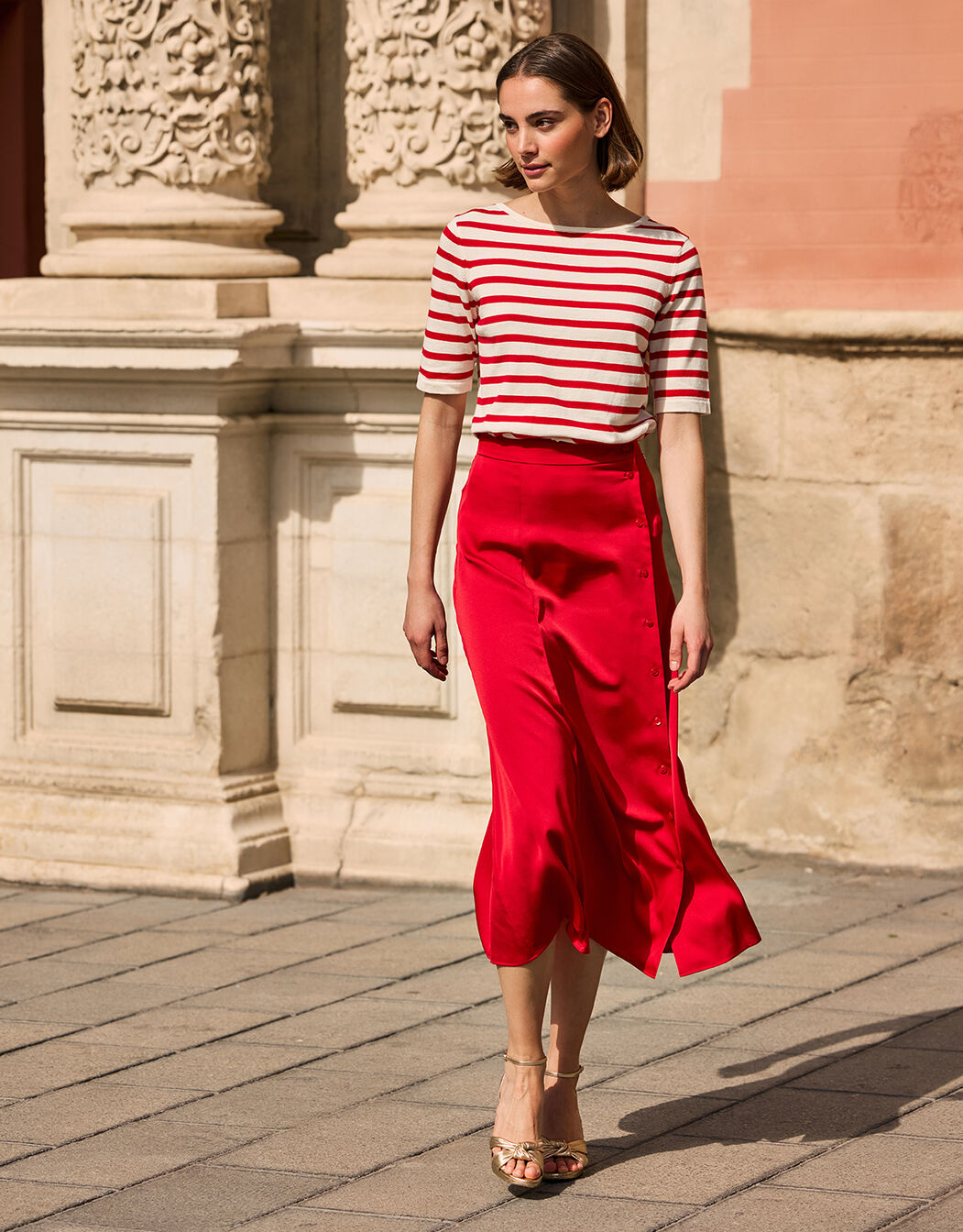 Model walking in the Helene Red skirt in satin with a red and white striped top.