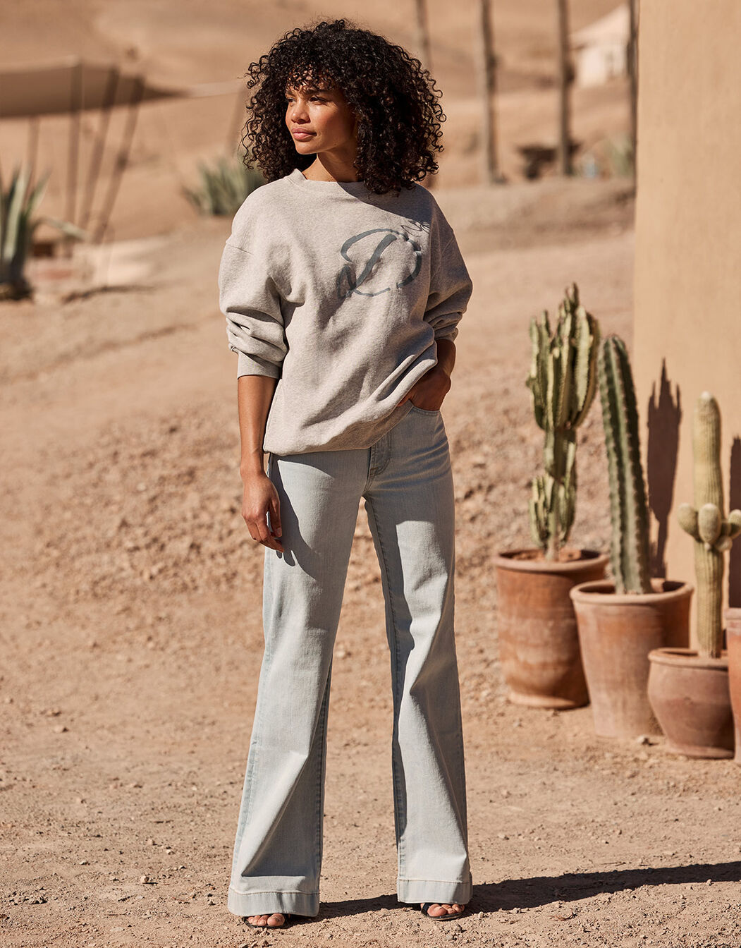 Model standing in the Candy Stone Grey Melange sweater in organic certified cotton with grey jeans.