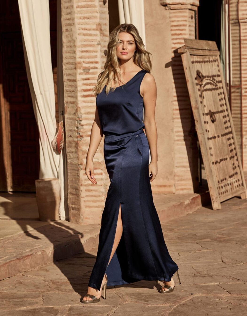 Model walking in the Selina Midnight Blue Satin skirt in crepe satin with a front slit.