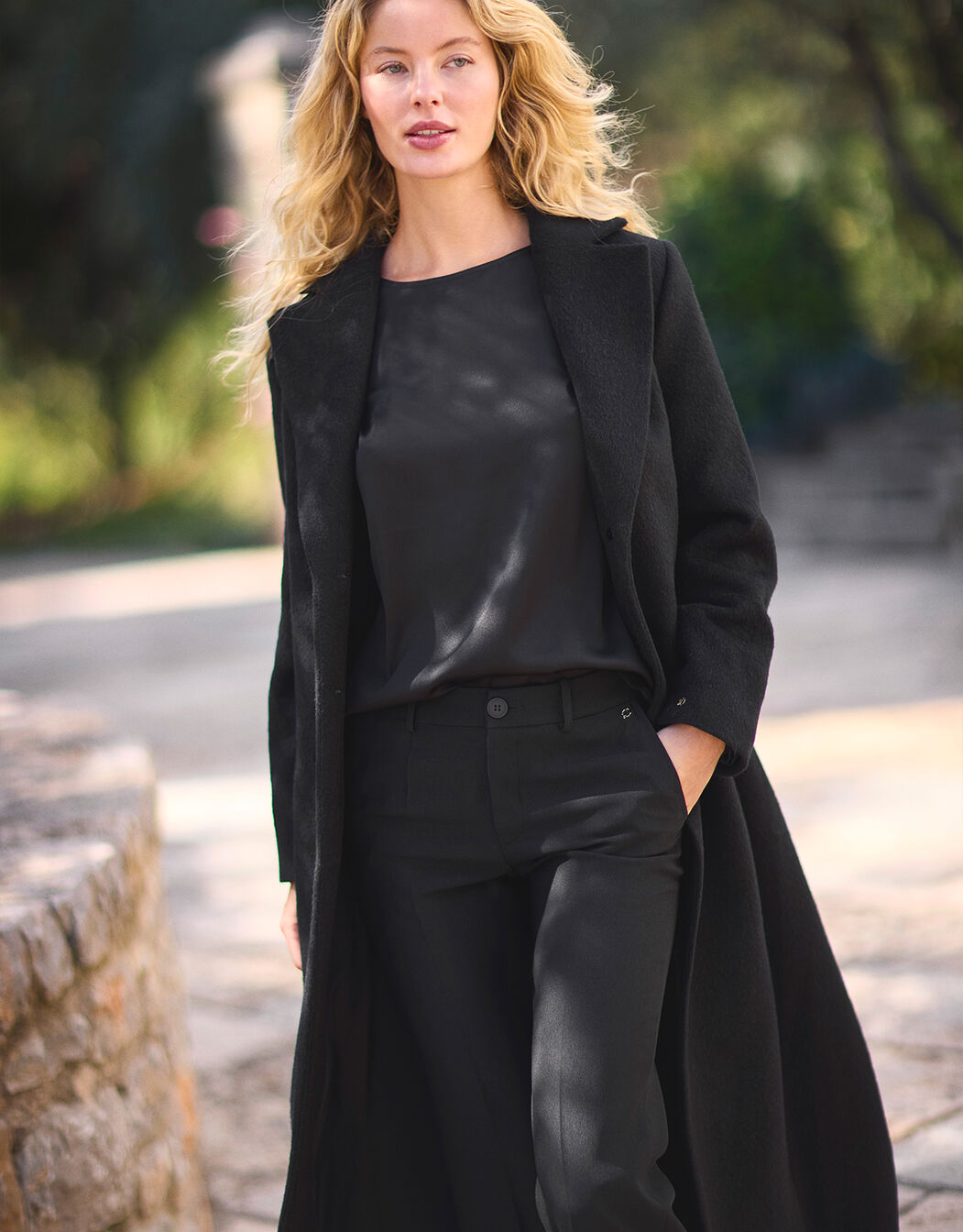 Model walking in the Noelle Black coat in wool blend, a long single-breasted style.