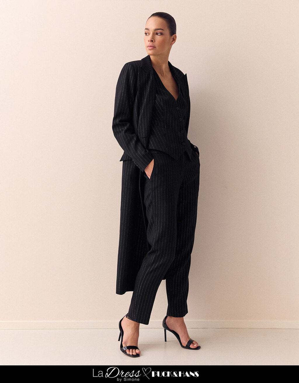 Woman wears elegant black pinstripe trousers with a matching blazer, a perfect business outfit in a modern style.