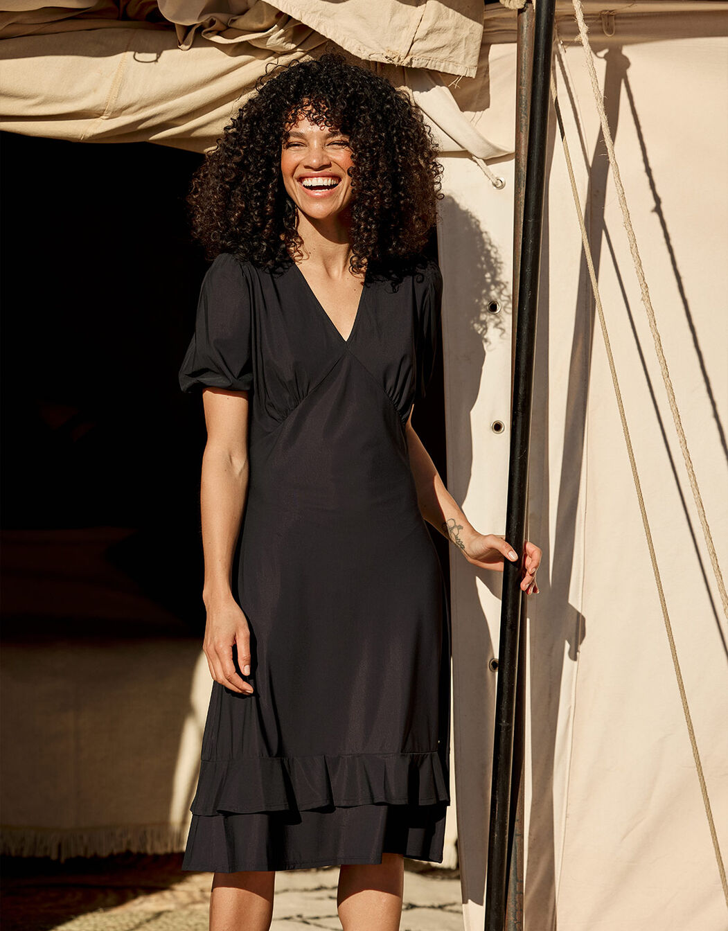 Model standing in the Kaya Black dress in jersey lycra with a V-neck and puff sleeves.
