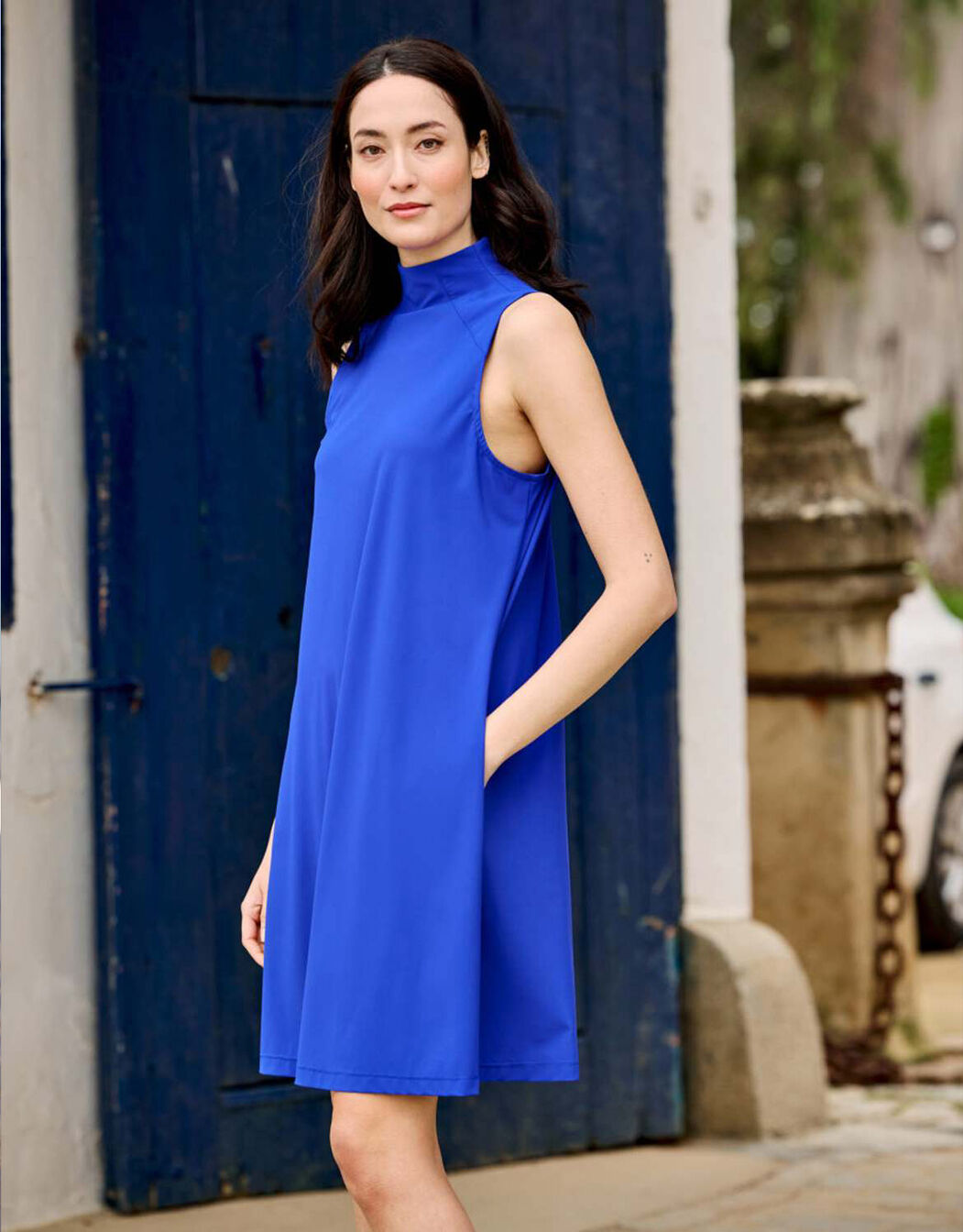 Model standing in the Celeste Marine Blue dress in jersey lycra, sleeveless with a stand collar.