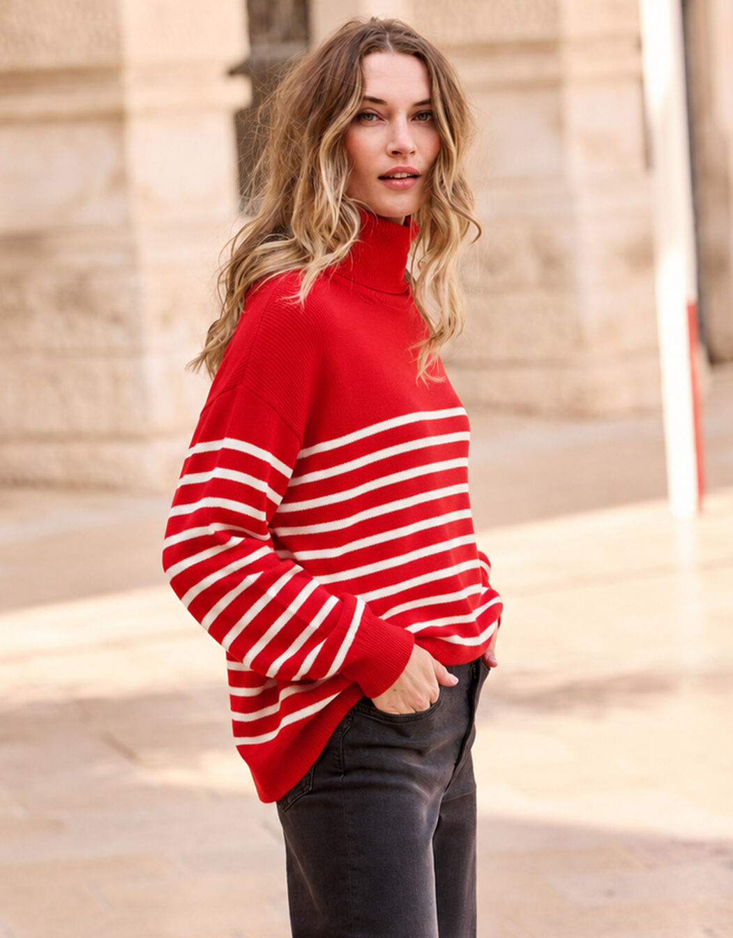 Model standing in the Cecile Red Ivory Stripe jumper in organic cotton knit with dark jeans.