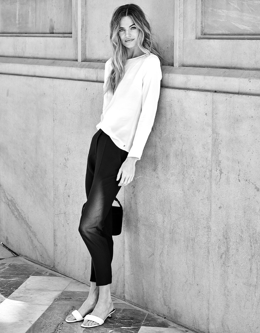 Model leaning in the Seoul Black trousers in crepe satin with a white blouse.